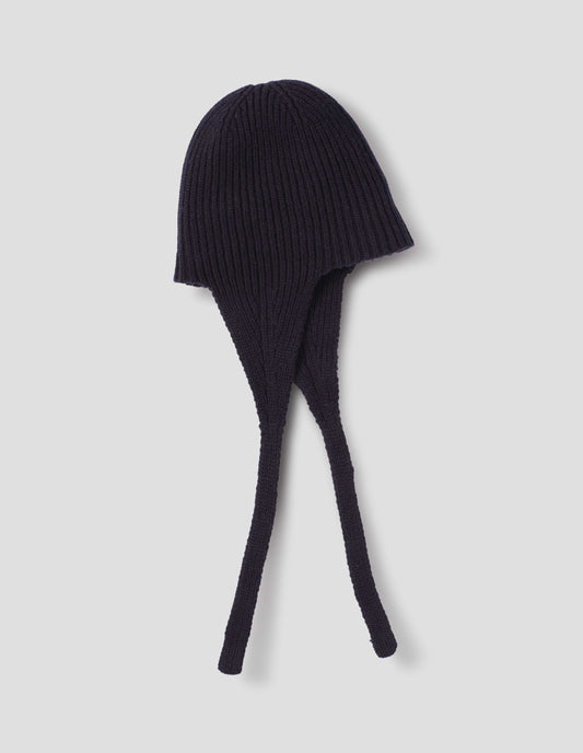 A navy blue rib knitted hat with ear flaps and tie detail, side flat lay view.