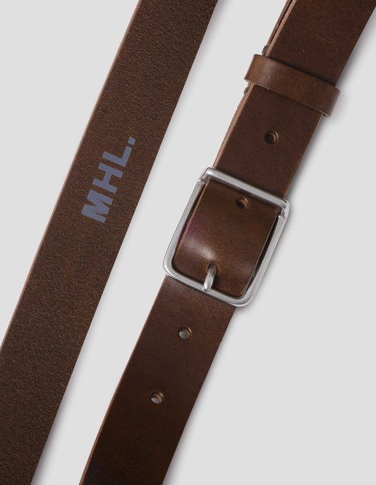 Dark brown leather belt with silver buckle, black leather strap and white MHL. logo stamped onto centre inside of belt. Close up detail flat lay view.