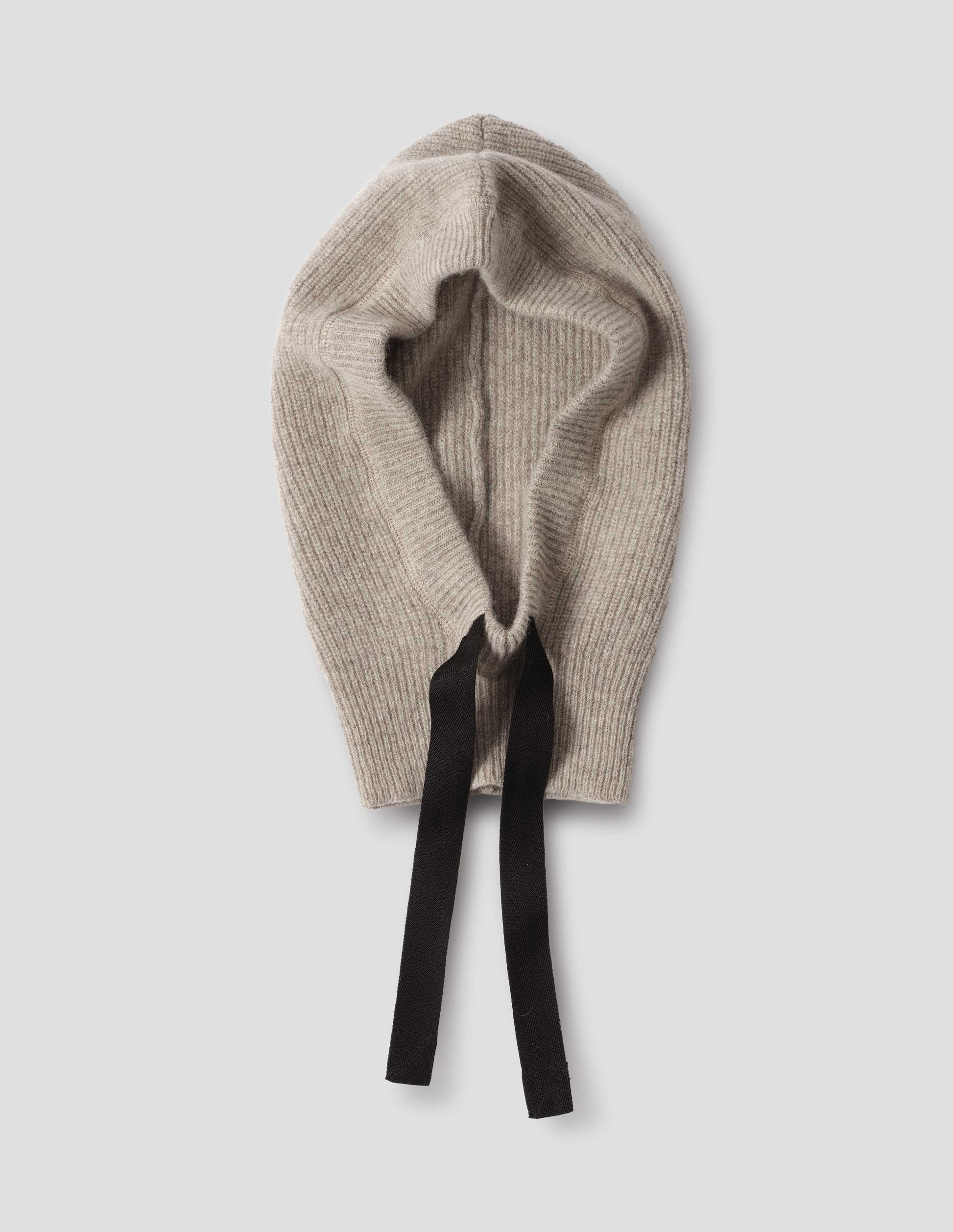 Beige knitted wool hood with contrasting black herringbone tape to adjust and contrast rib on face, front flat lay view.
