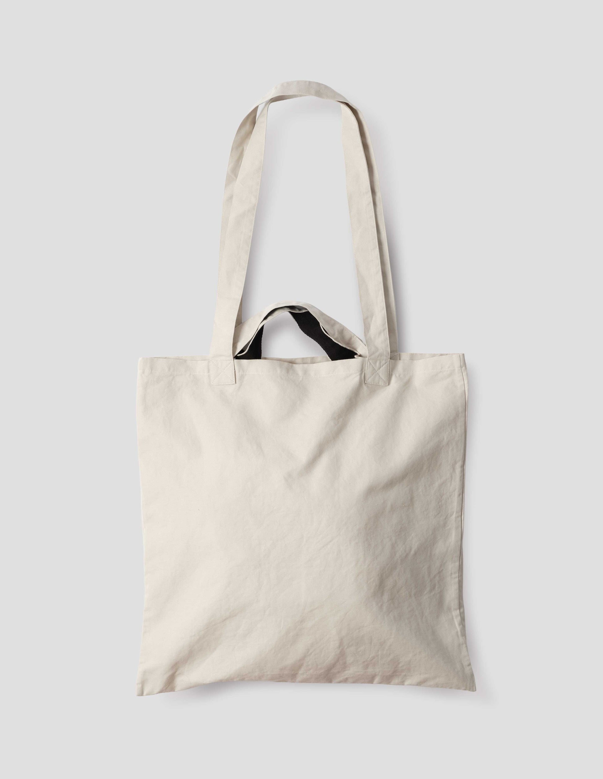 Beige cotton linen tote bag with long and contrasting black short handles. Back flat lay view. 