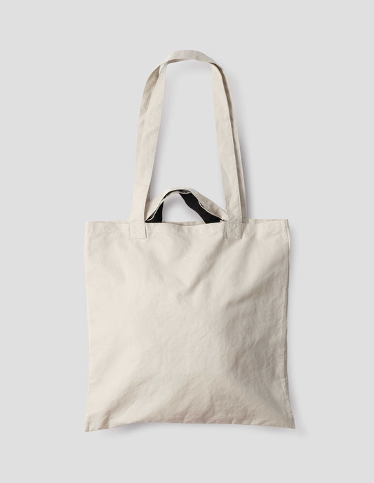 Beige cotton linen tote bag with long and contrasting black short handles. Back flat lay view. 
