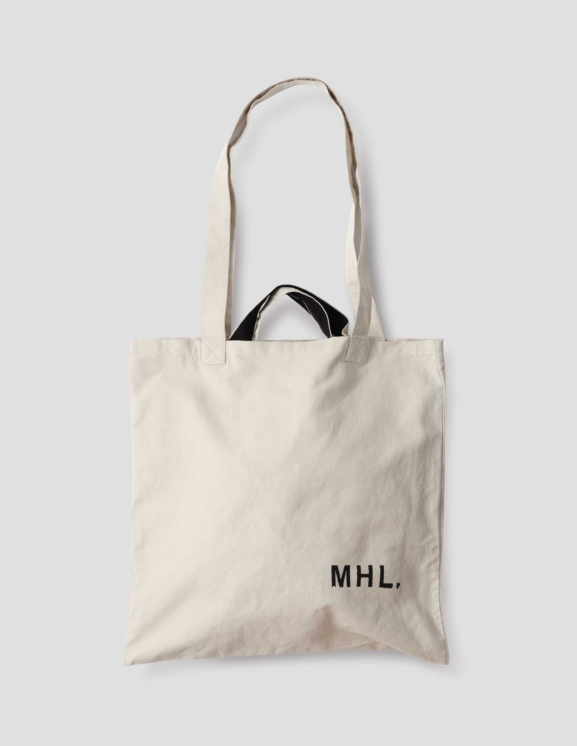 Beige cotton linen tote bag with long and contrasting black short handles, with MHL. branding logo in bottom right corner. Front flat lay view. 