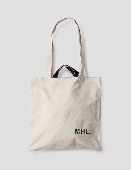 Beige cotton linen tote bag with long and contrasting black short handles, with MHL. branding logo in bottom right corner. Front flat lay view. 