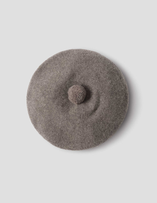 Greyish beige wool tam o shanter hat with matching pom pom bobble in centre. View from above flat lay view.