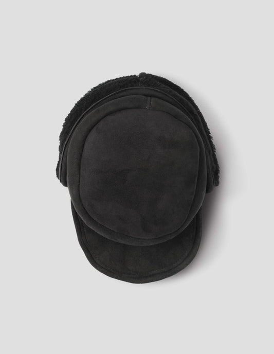 Black shearling press stud cap with peak and black curly merino sheepskin ear flaps. View from above flat lay.