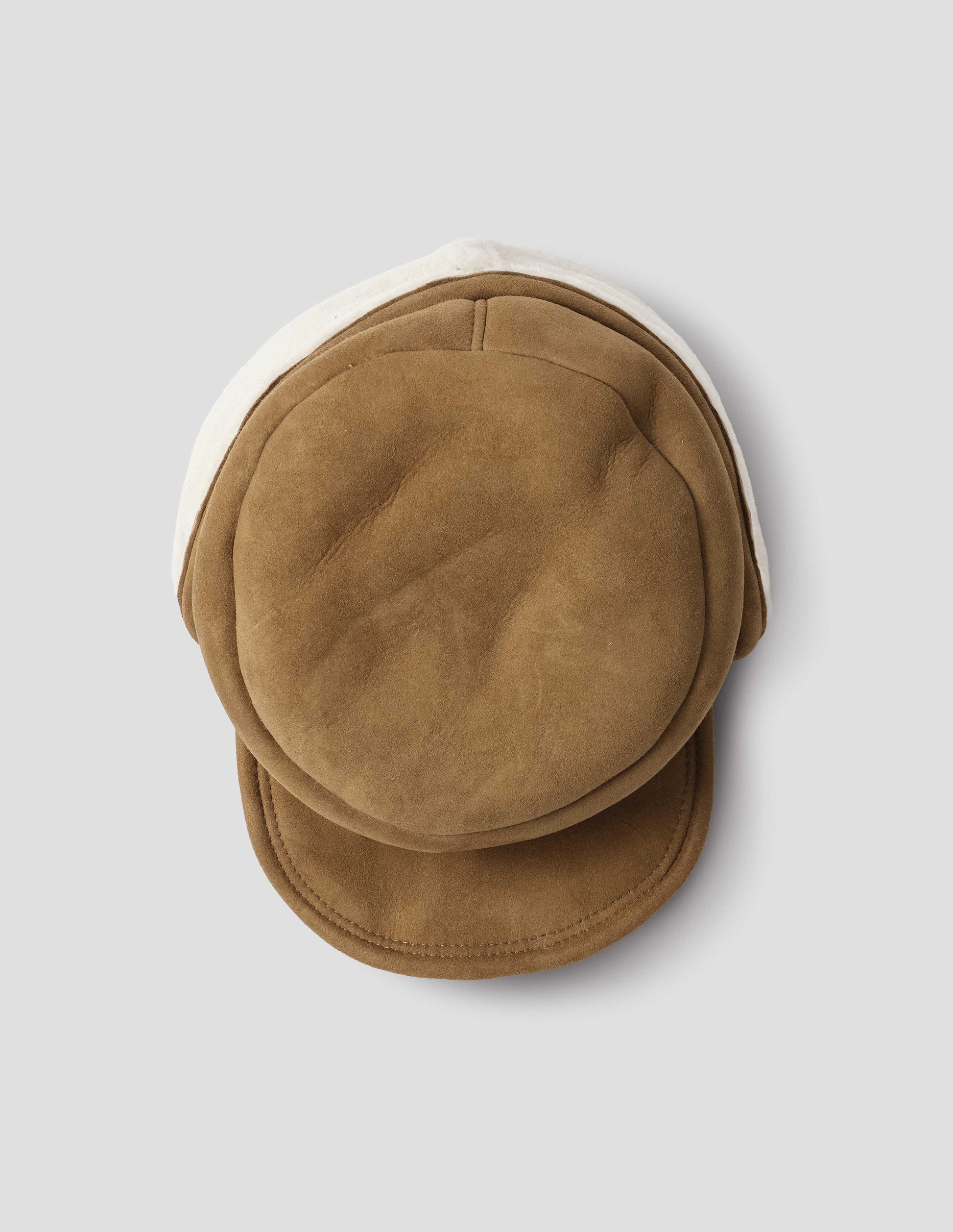 Light brown shearling press stud cap with peak and white curly merino sheepskin ear flaps. View from above flat lay.