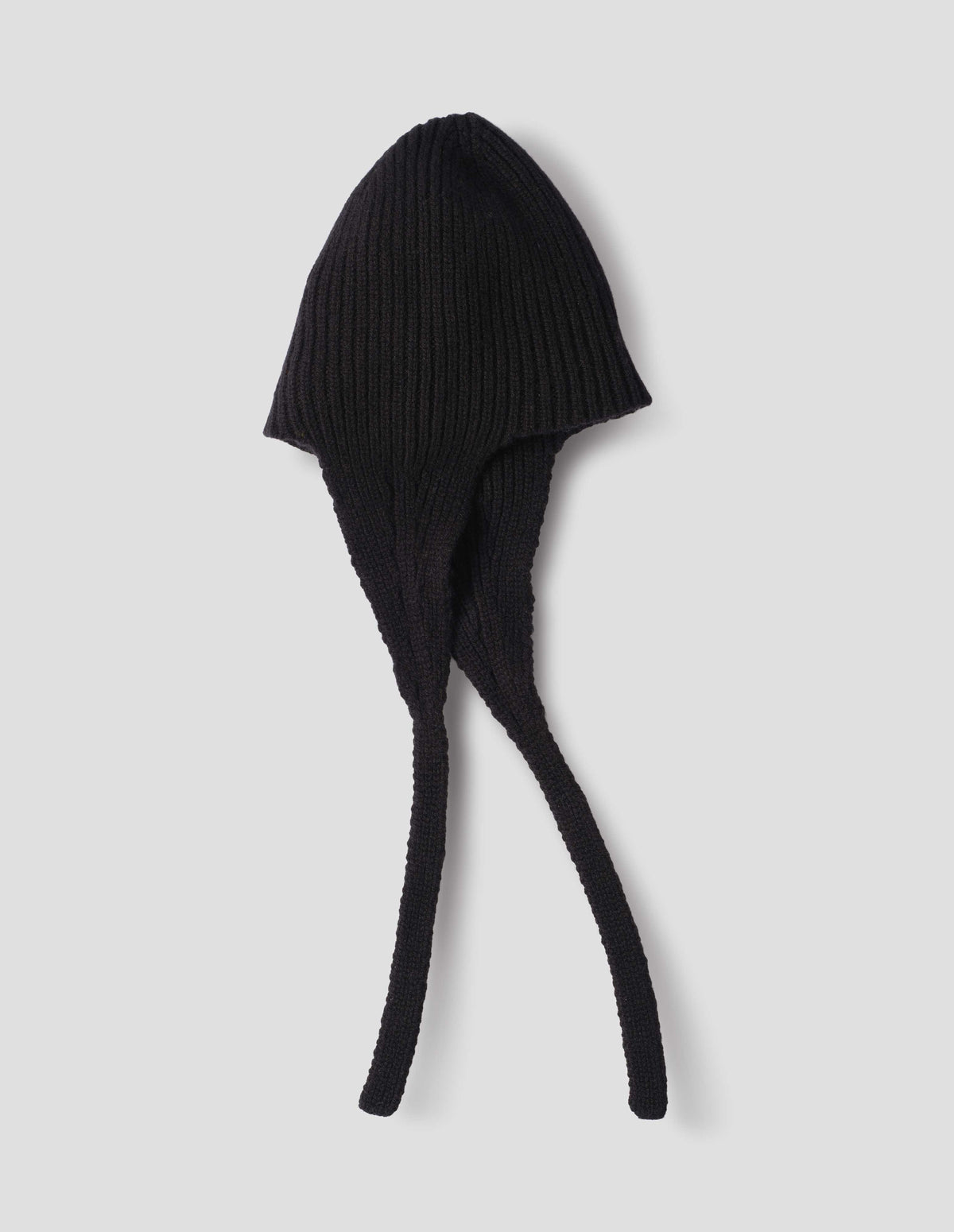 Black soft spun merino knitted ribbed hat with ear flaps and tie detail. Side flat lay view.