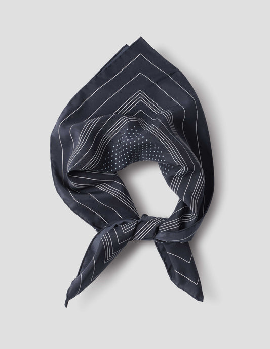 Dark blue folded and tied silk neck scarf with white stripes and dots, and hand rolled edges. Close up flat lay view.