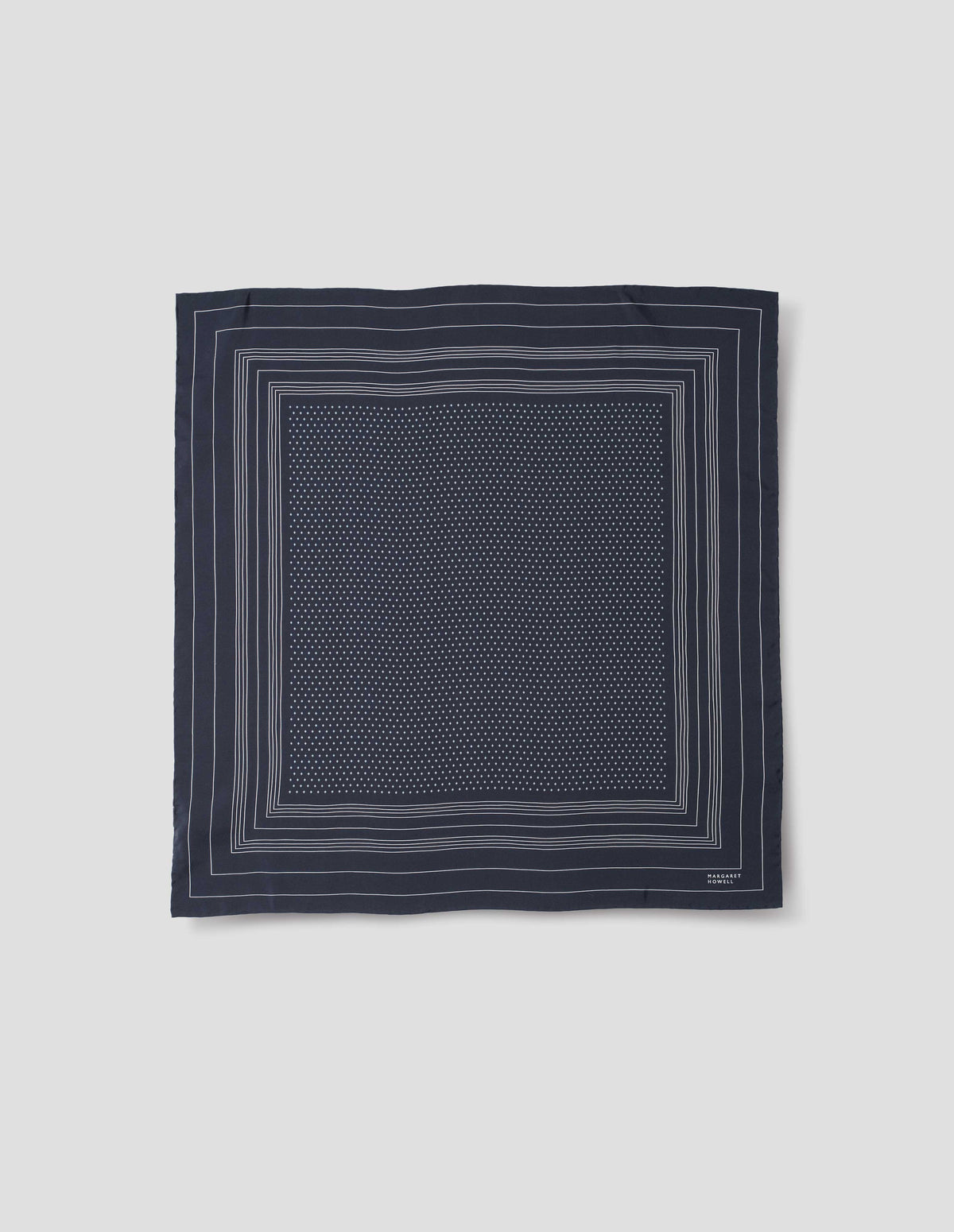 Dark blue square silk neck scarf with white border stripes with white dots inside hand rolled edges and white Margaret Howell logo in right corner. Front flat lay view.