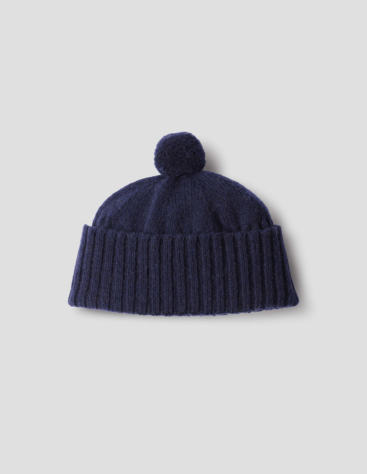 Dark blue knitted Shetland wool bobble hat with rib turned up cuff, front flat lay view.
