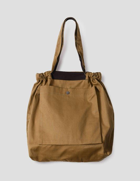Light brown tote bag with matching drawn up handles, large press stud fastening bellows patch pocket and contrasting herringbone tape detailing. Front flat lay view.