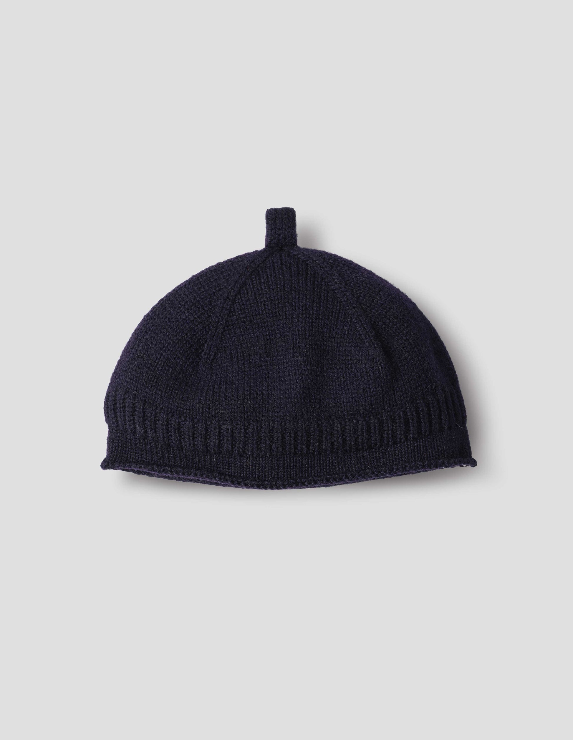 Dark blue merino wool beanie hat with a band of contrasting rib rolled edge brim and knitted loop detailing on top, front flat lay view.