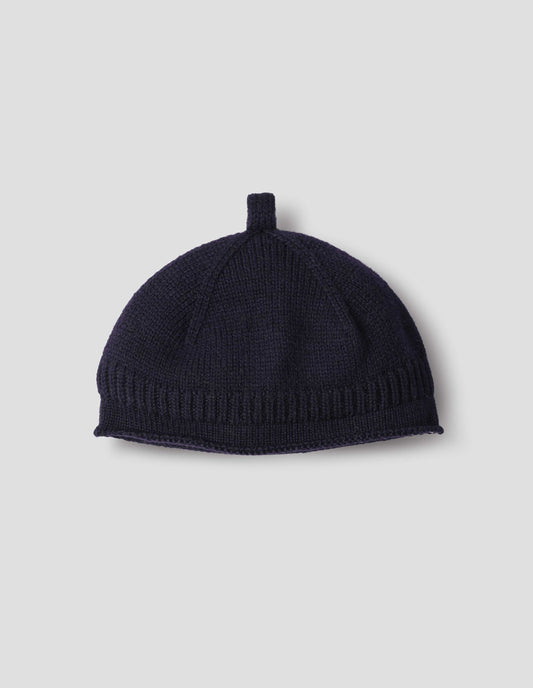 Dark blue merino wool beanie hat with a band of contrasting rib rolled edge brim and knitted loop detailing on top, front flat lay view.