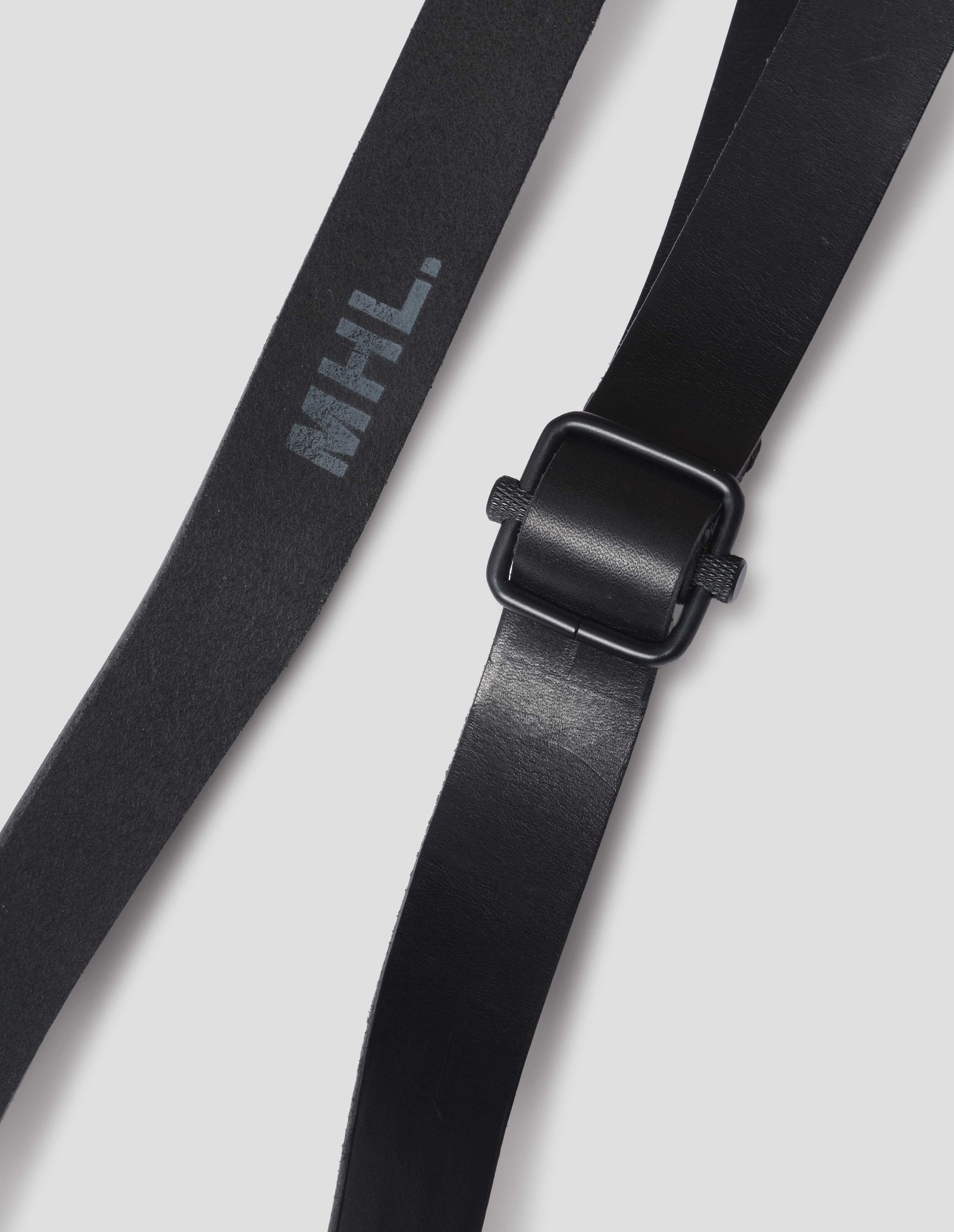 Black leather belt, detail of reverse of leather with MHL logo and square black slider buckle, close up view.