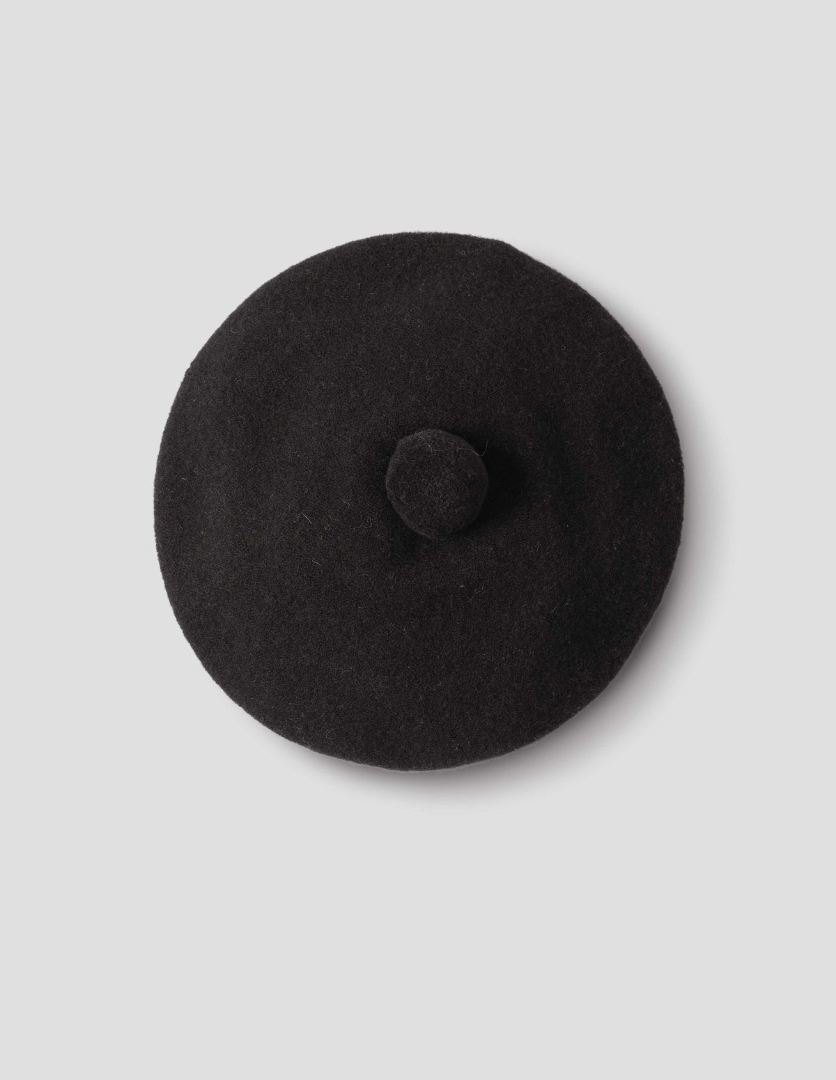 Black wool tam o shanter hat with matching pom pom in centre, from above flat lay view.