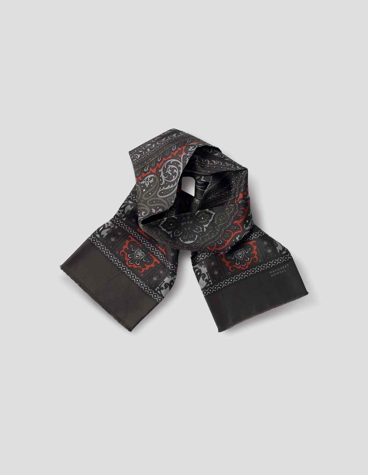 Dark green double sided silk scarf with orange, green and light blue paisley print, frayed edges and contrast Margaret Howell logo. Front flat lay view.