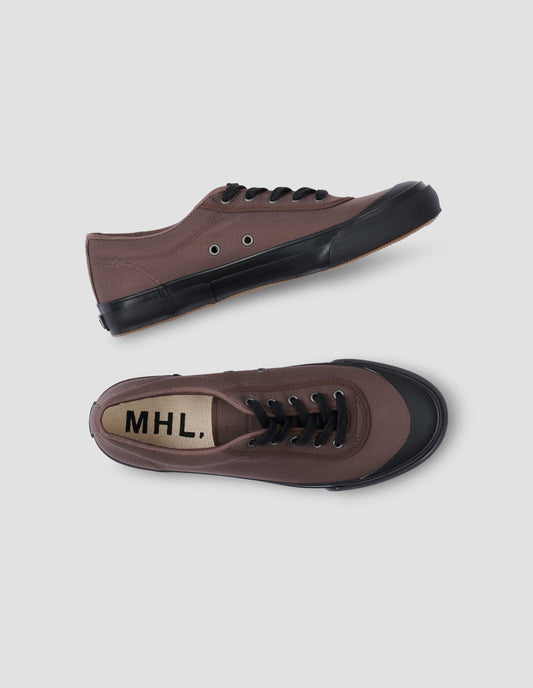 A pair of brown cotton canvas trainers with metal eyelet, black laces and contrast vulcanised rubber sole. View from above flat lay view.