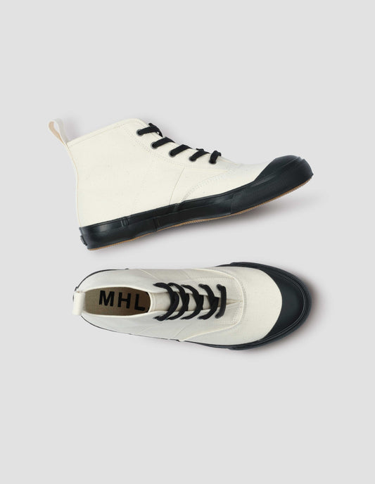 Off white high top canvas trainers with metal eyelets, contrasting black laces, canvas heel loop and contrasting black rubber sole. View from above flat lay.