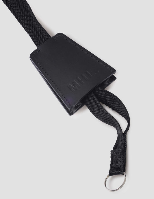 Black full grain leather key holder with contrasting black cotton strap and embossed MHL. logo on front of holder. Close up detail flat lay.