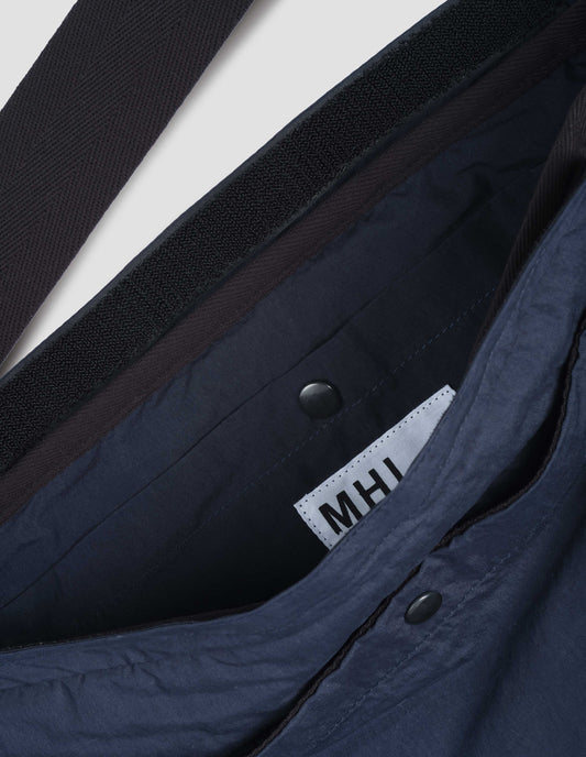 Navy blue bag with contrast black herringbone tape shoulder strap and Velcro closure. Fabric swatch.