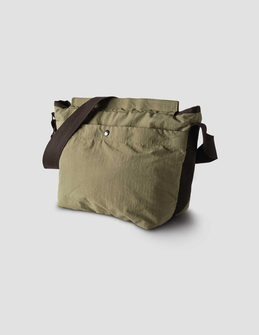 Khaki green bag with contrast black herringbone tape shoulder strap, large popper fastening pocket and Velcro closure. Side flat lay view. 