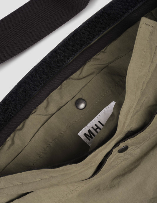 Khaki green bag with contrast black herringbone tape shoulder strap and Velcro closure. Fabric swatch.