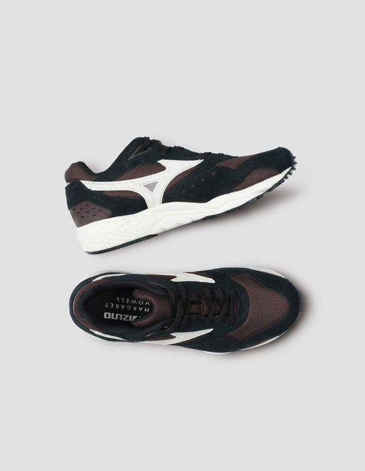 A pair of black and dark brown suede trainers with mesh insert and off white sole, with off white Mizuno logo running through the side. View from above flat lay.