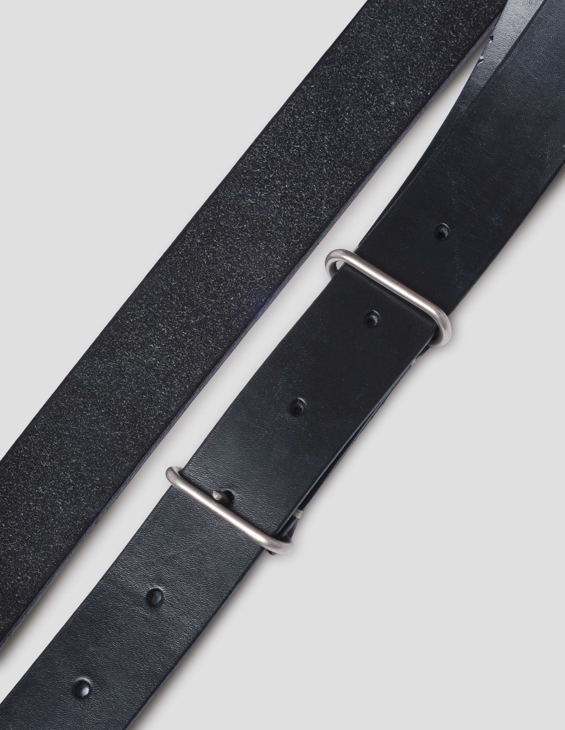 Detail of the silver coloured buckle and keeper showcasing the top and flesh sides of the leather with punched holes. Close up view.