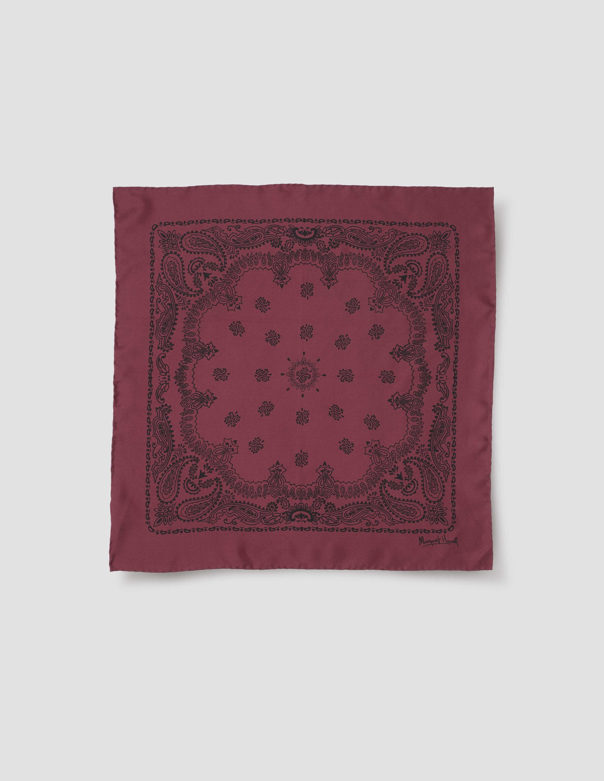 Dark pinkish red square neck scarf with contrast black paisley pattern and Margaret Howell signature in bottom right corner. Front flat lay view.