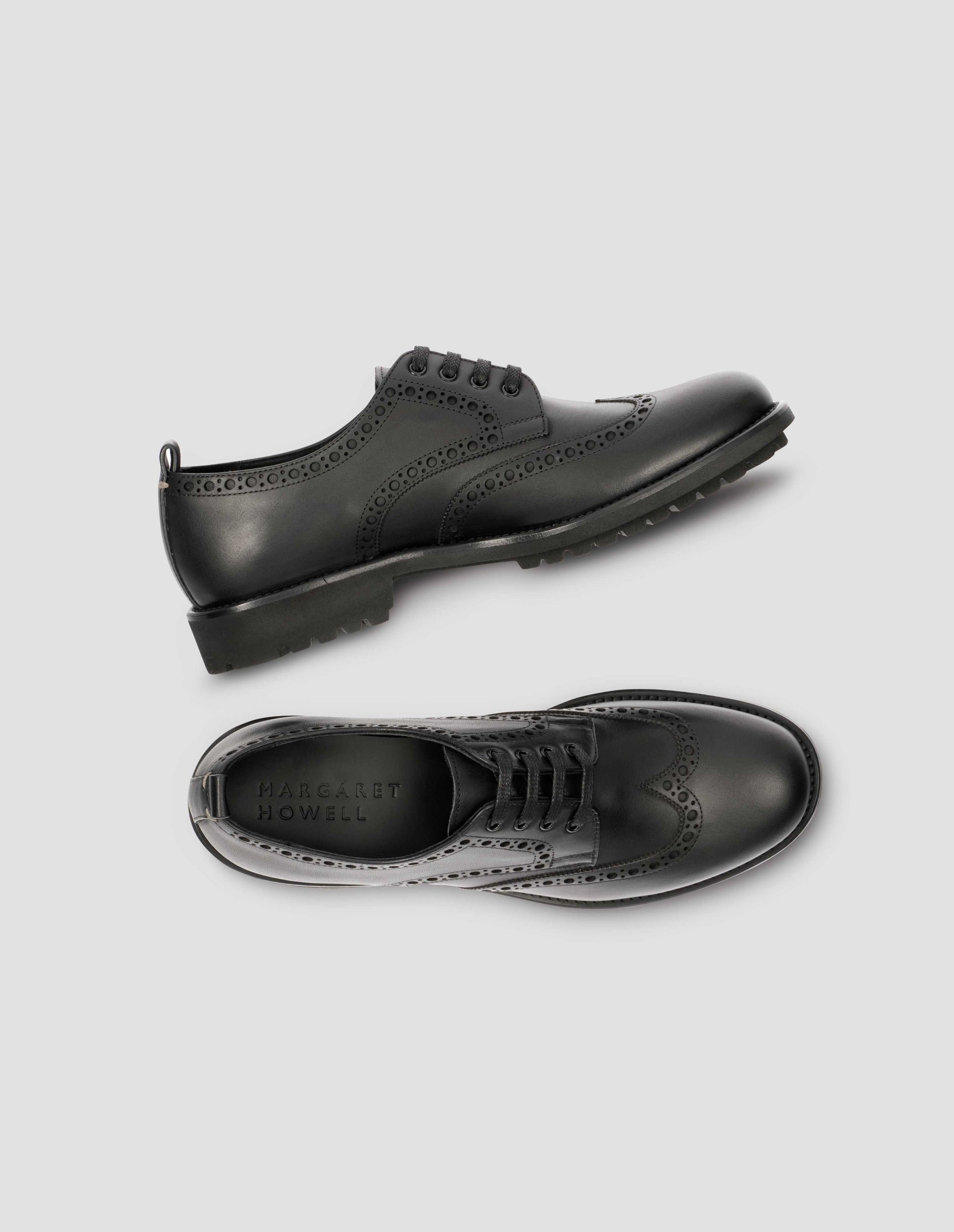A pair of matt black leather brogues with black laces and lightweight rubber commando sole. View from above flat lay.