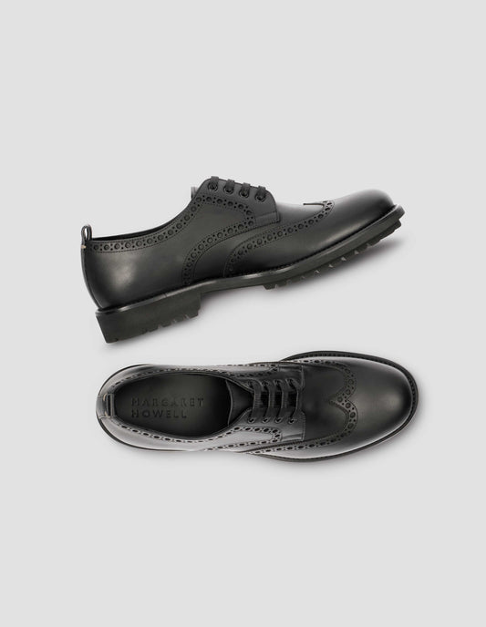 A pair of matt black leather brogues with black laces and lightweight rubber commando sole. View from above flat lay.