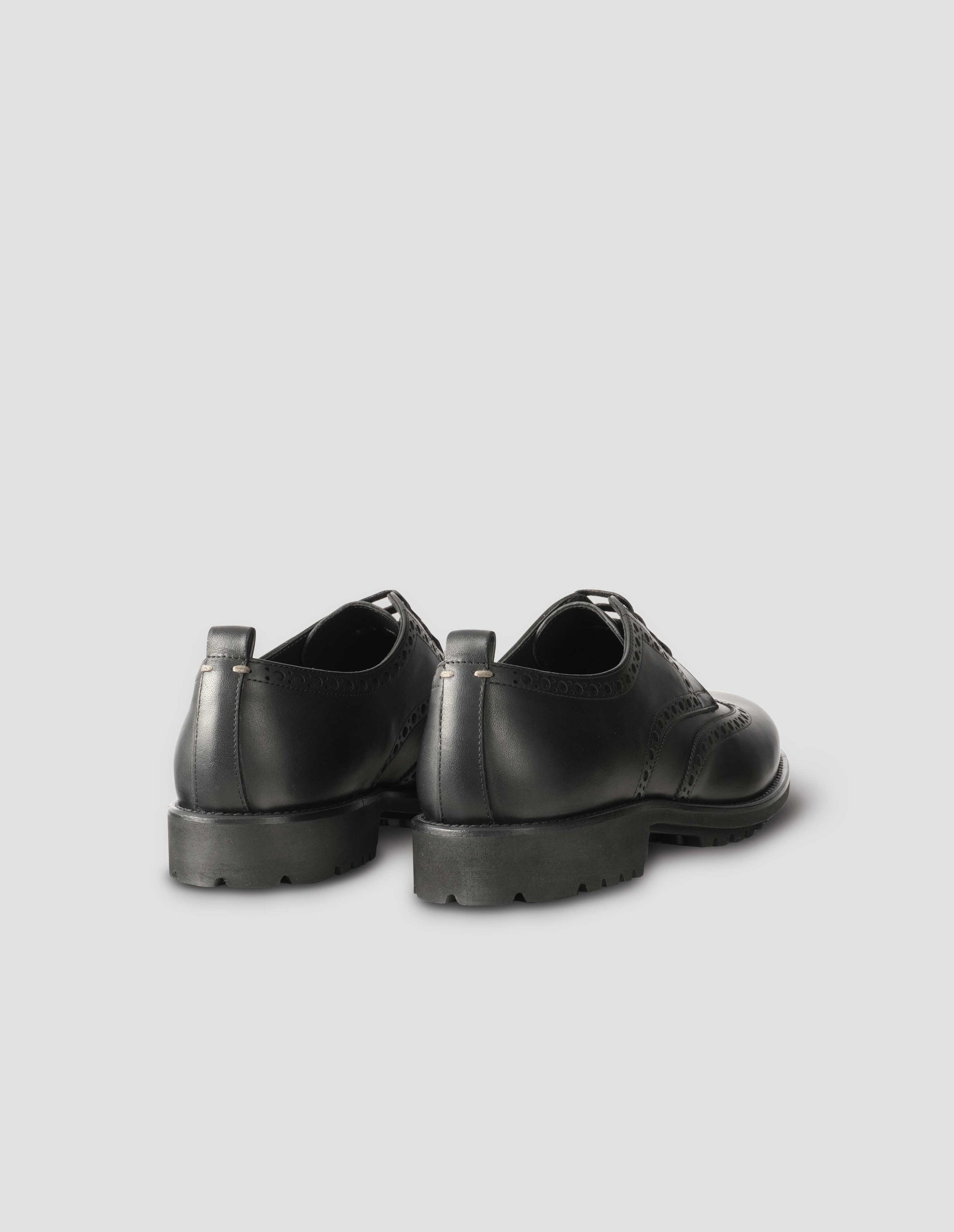 A pair of matt black leather brogues with black laces and lightweight rubber commando sole. Back flat lay