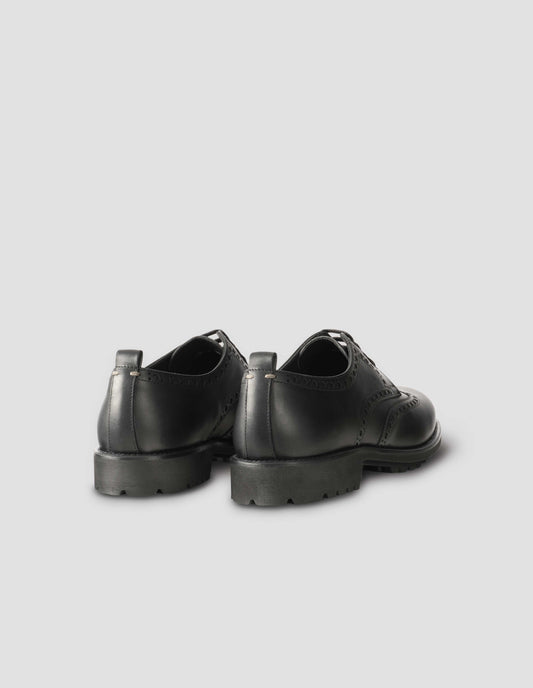 A pair of matt black leather brogues with black laces and lightweight rubber commando sole. Back flat lay