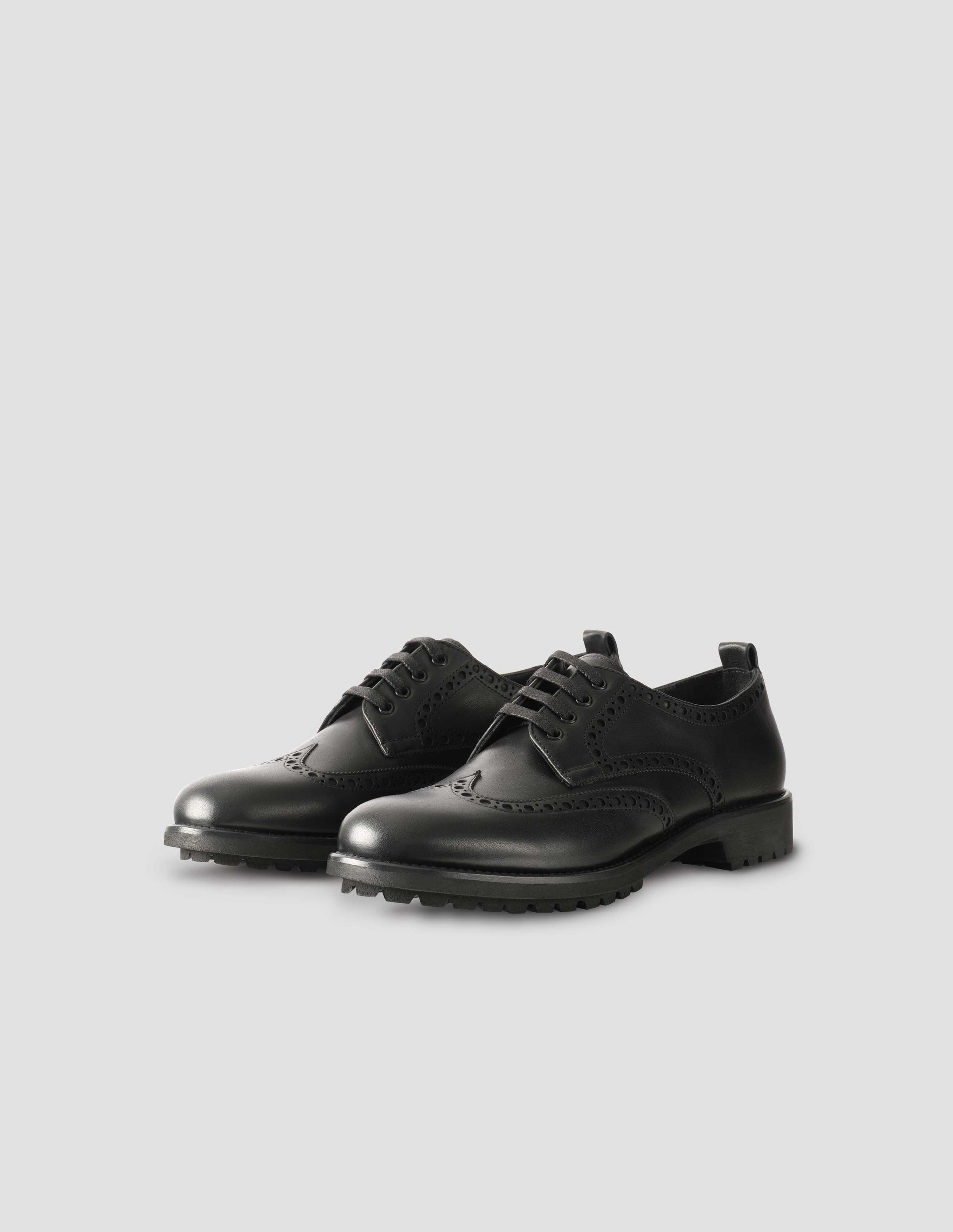 A pair of matt black leather brogues with black laces and lightweight rubber commando sole. Side view flat lay