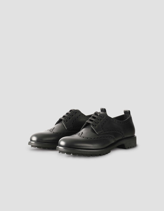 A pair of matt black leather brogues with black laces and lightweight rubber commando sole. Side view flat lay
