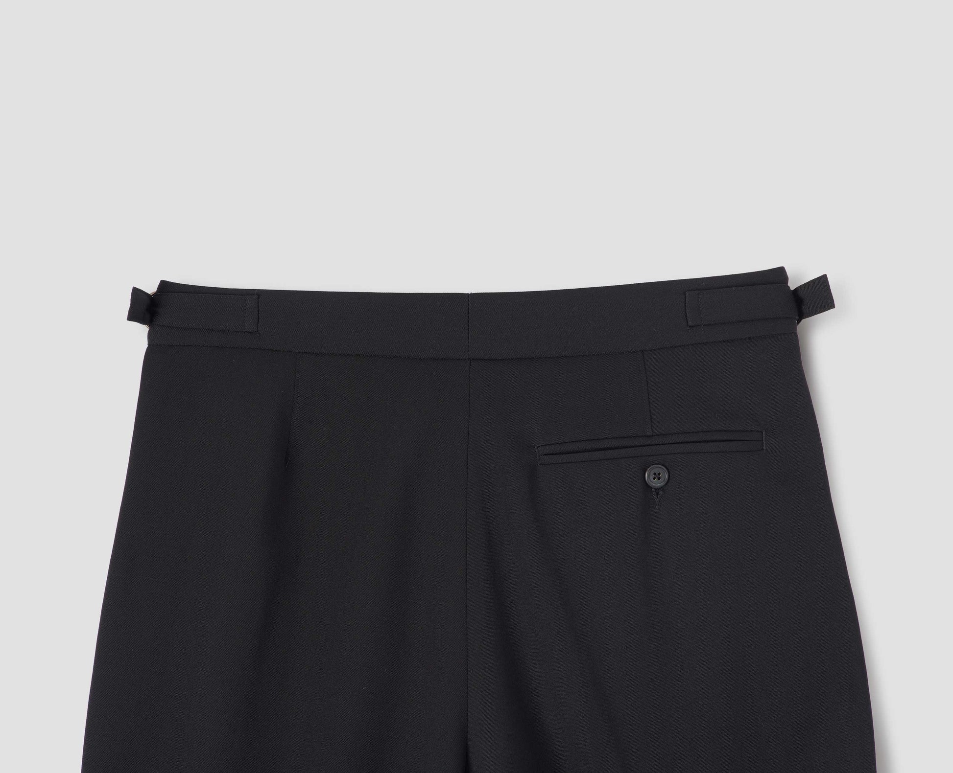 Black wool wide leg trousers, with D ring waist adjusters and button through jet back pocket. Back flat lay view.