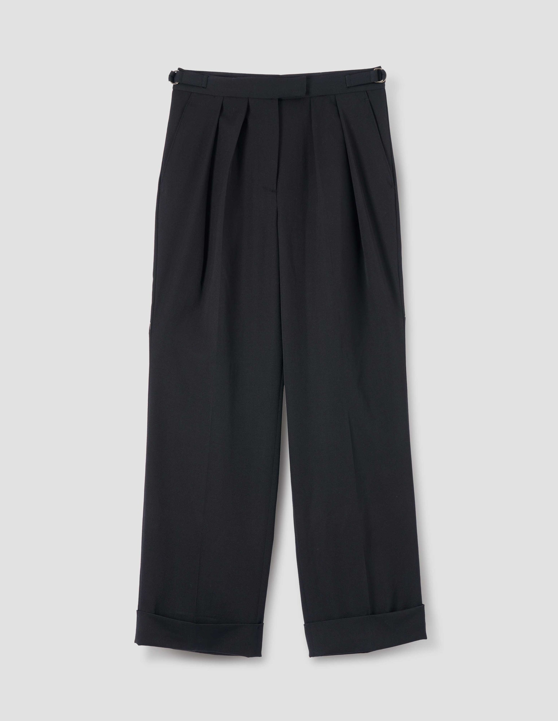 Black wool wide leg trousers, with twin pleats, zip front with hook and bar fastening, D-ring waist adjustors, slant pockets and turned up hems. Front flat lay view. 