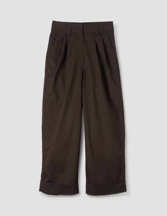 Dark brown pleated trousers with zip fly and double hook and bar fastening, slant side pockets and turn up hems. Front flat lay view.
