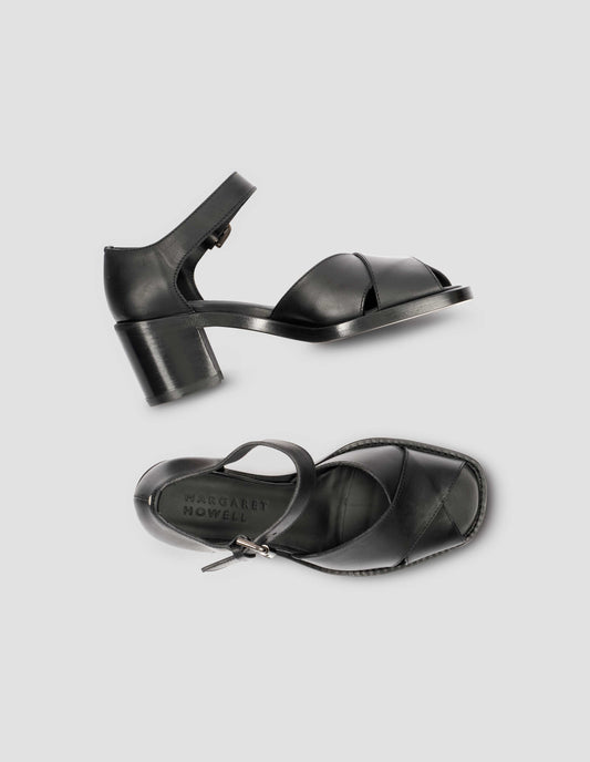 A pair of black leather open toe heels with buckle fastening. View from above flat lay.