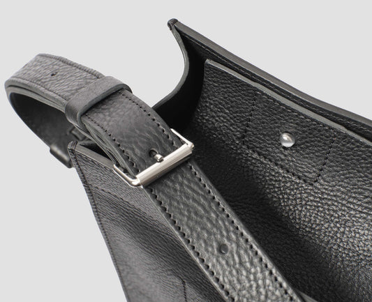 Black fine grain leather tote bag with a roller buckle adjustable shoulder strap and stud fastening closure, fabric swatch.