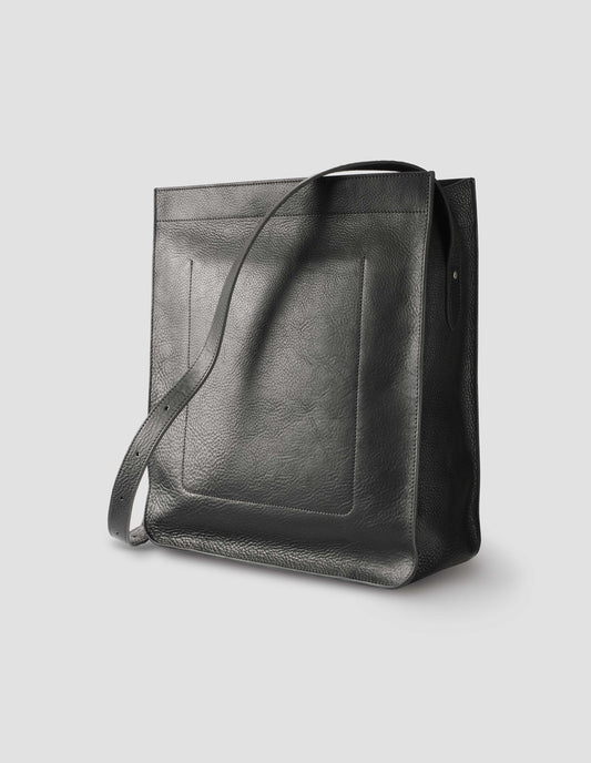 Black fine grain leather tote bag with a roller buckle adjustable shoulder strap, large internal stitch-through sleeve pocket and hand-stained turned-out seams. Back side view flat lay.