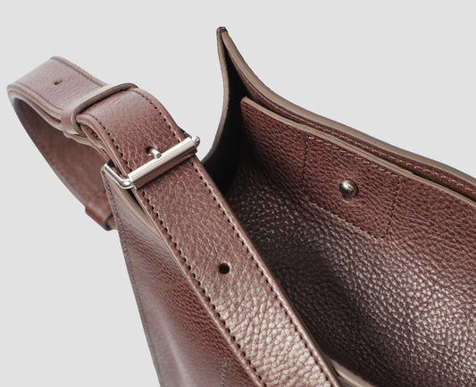 Brown fine grain leather tote bag with a roller buckle adjustable shoulder strap and stud fastening closure, fabric swatch.