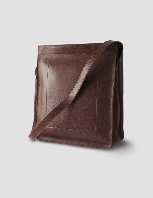 Brown fine grain leather tote bag with a roller buckle adjustable shoulder strap, large internal stitch-through sleeve pocket and hand-stained turned-out seams. Back side view flat lay.