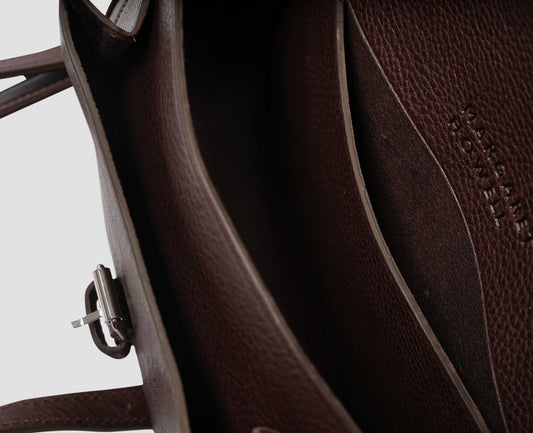 Brown  fine grain leather small satchel bag with pleat expandable exterior pocket and interior slip pocket and embossed Margaret Howell logo detail. Fabric swatch.