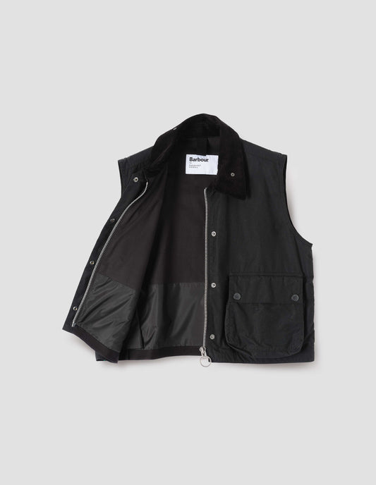 Black cotton drill lined boxy gilet with storm tab on corduroy collar, two-way zip fastening and press stud fastening storm flap, large bellows pockets with press stud fastening envelope closure. Open flat lay view.