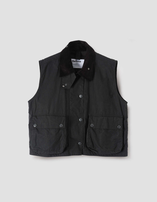 Black boxy gilet with storm tab on corduroy collar, press stud fastening storm flap, large bellows pockets with press stud fastening envelope closure. Front flat lay view.