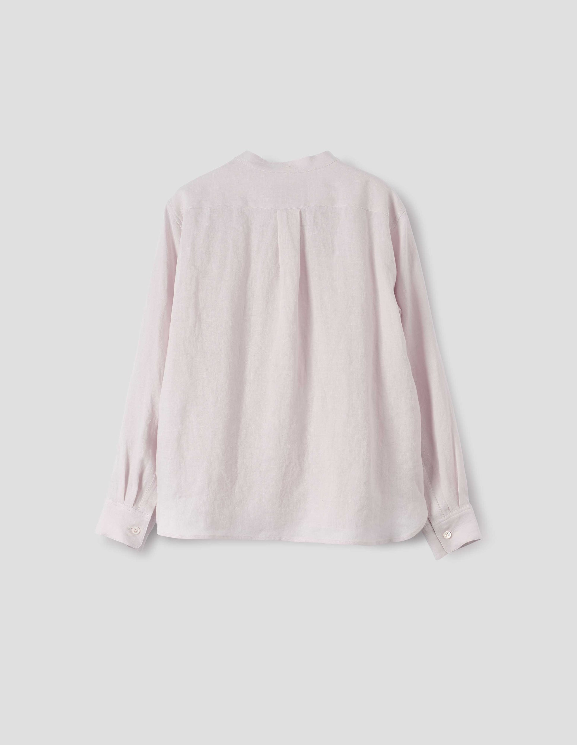 Pinkish beige collarless shirt, with mother of pearl button cuffs, box stitch detailing on back yoke and elongated hem. Back flat lay view.