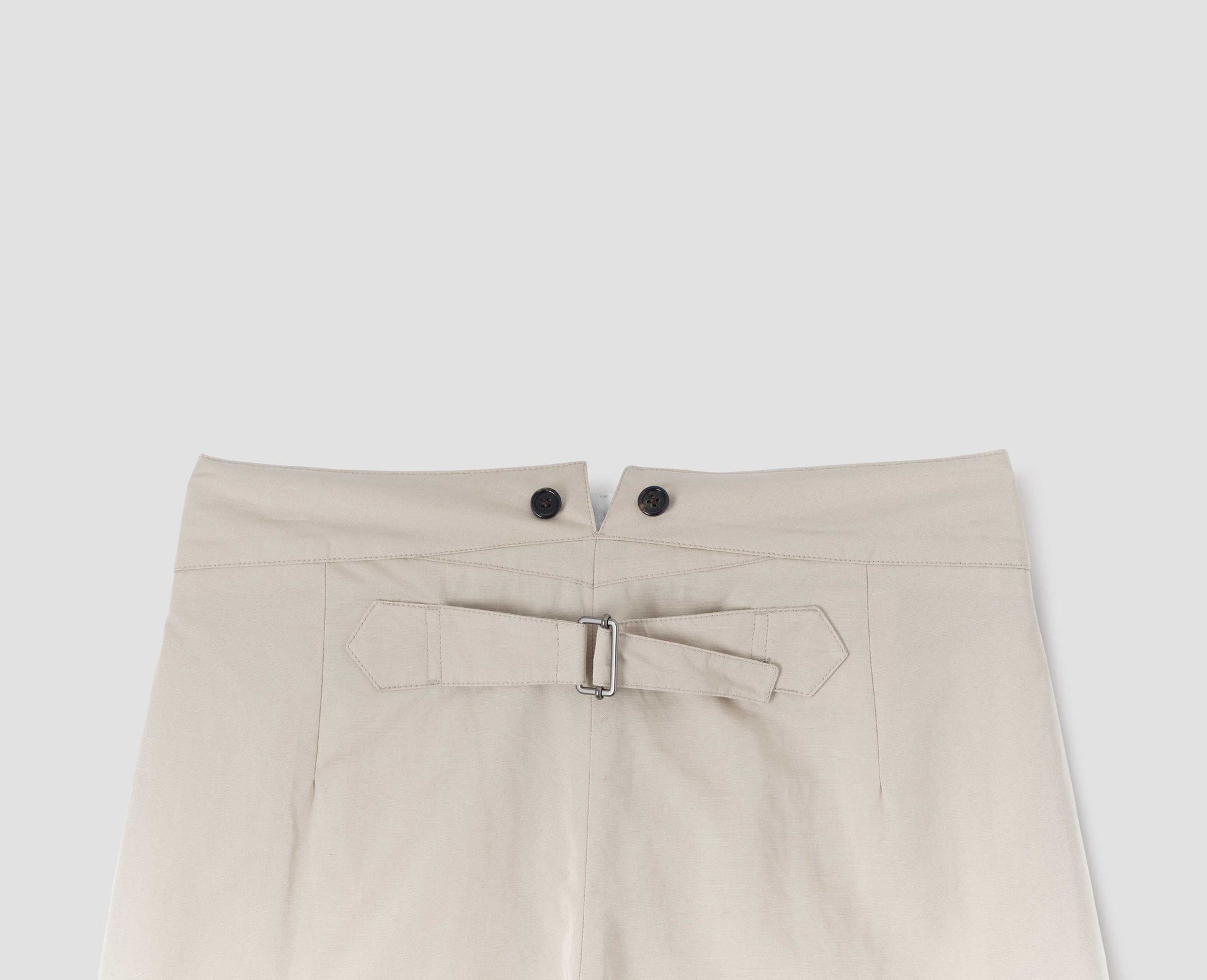 Beige high waisted trousers with double black horn button details on waistband and cinch back, back flat lay view. 