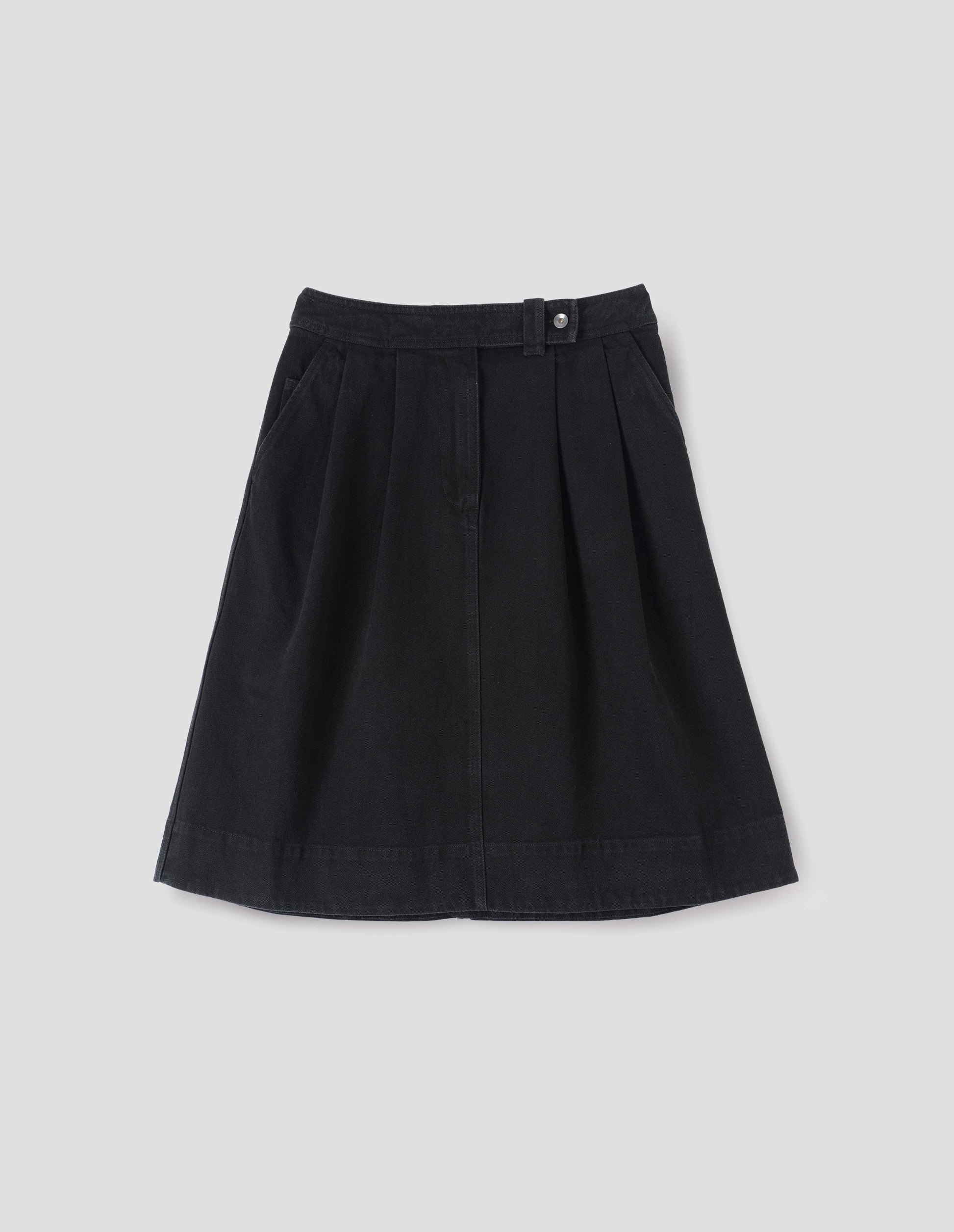 Black A-line skirt with pleats, denim button fastening and zip fly, slant pockets with ticket pocket detail, front flat lay view.