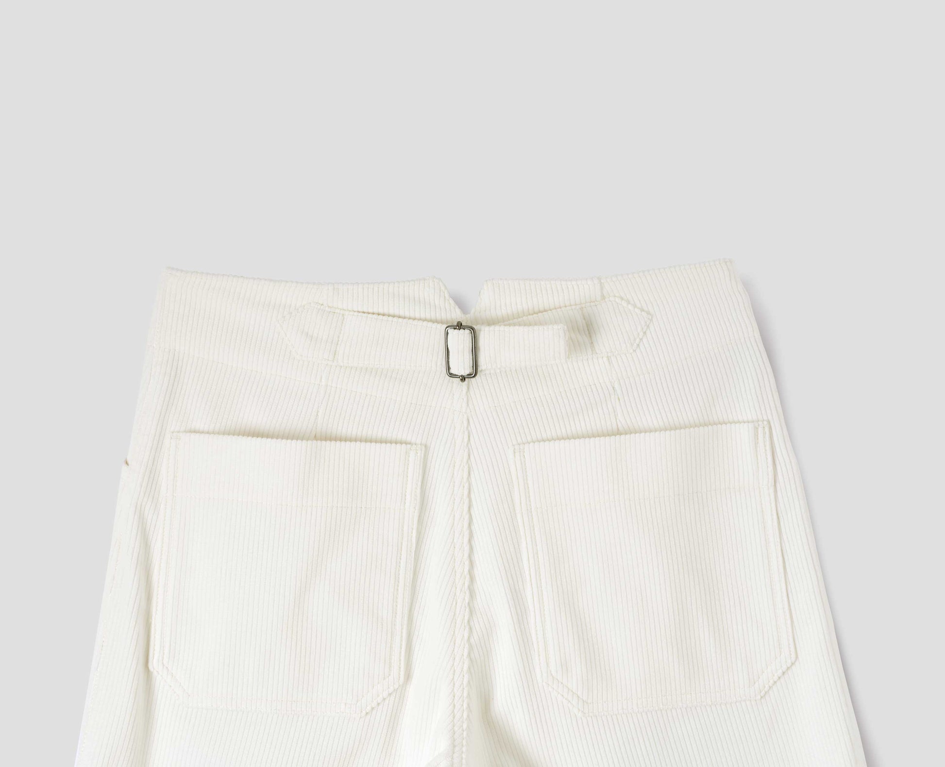 White heavy corduroy trousers with deep stitch-through hem, patch back pockets and cinch waist adjusters. Back flat lay view.